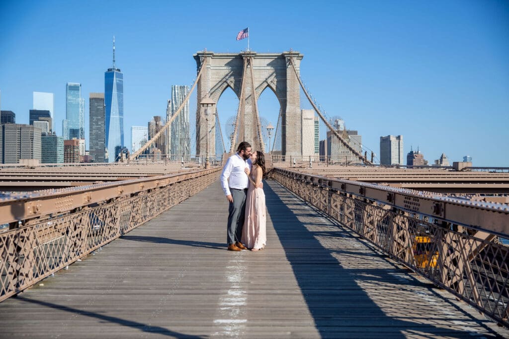 An engaged couple kiss on the Brooklyn Bridge.