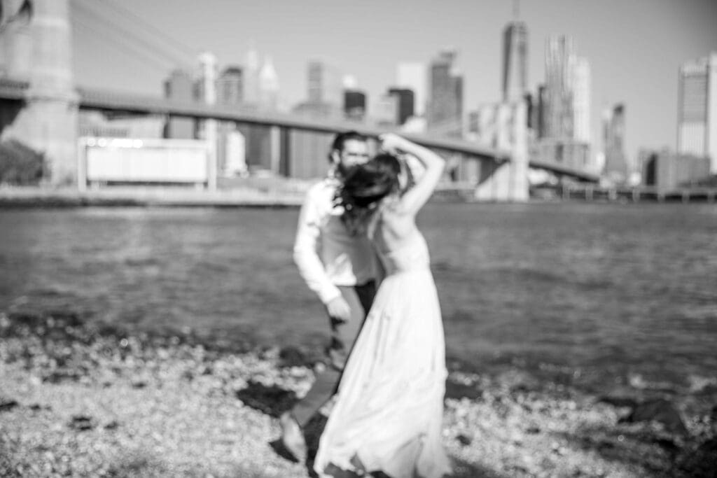 An engaged couple dance in Pebble Beach in Dumbo, Brooklyn, NYC with the bridge and Manhattan skyline behind them.