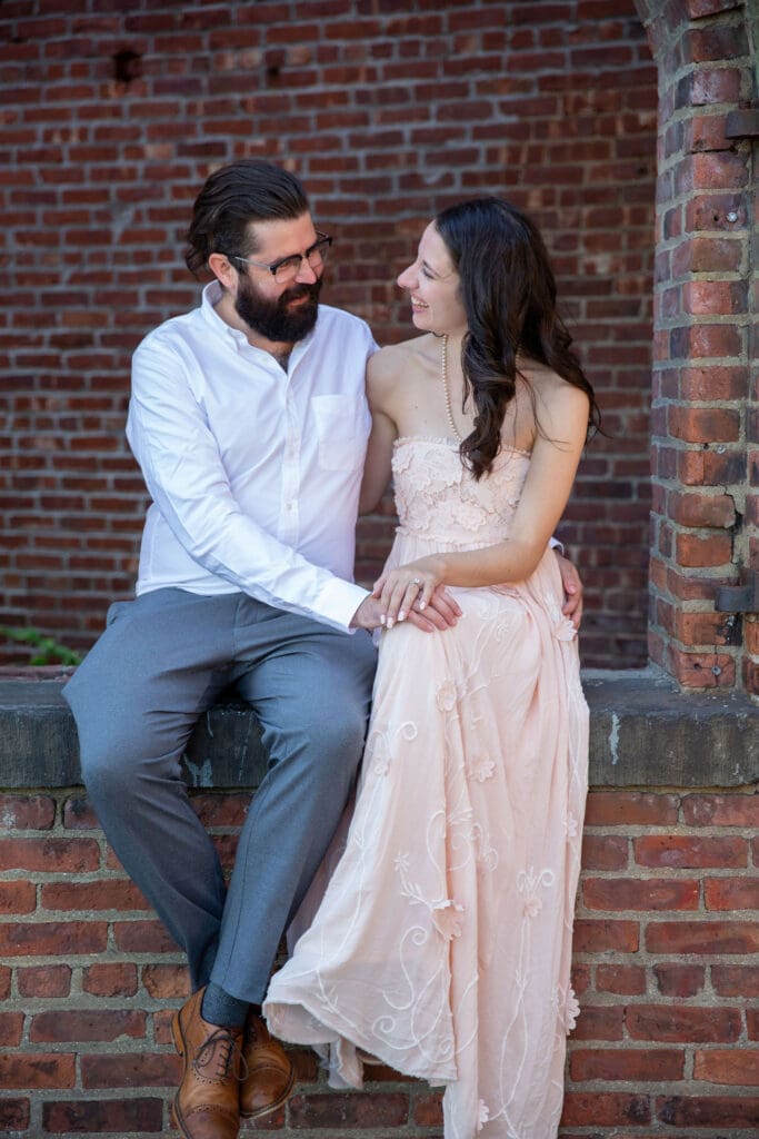 An engaged couple embrace and laugh at the red bricks at Max's Garden in Dumbo, Brooklyn, NYC.