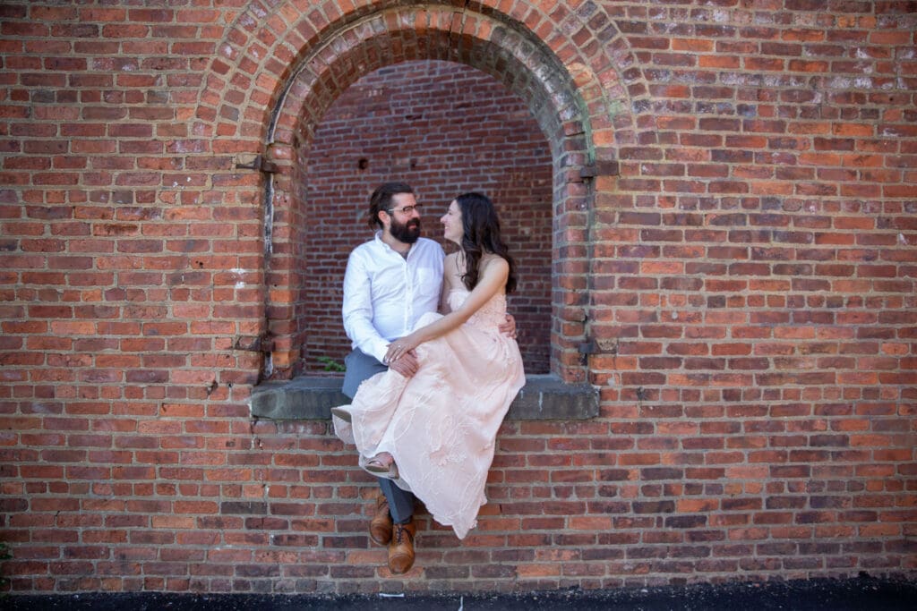 An engaged couple embrace and laugh at the red bricks at Max's Garden in Dumbo, Brooklyn, NYC.