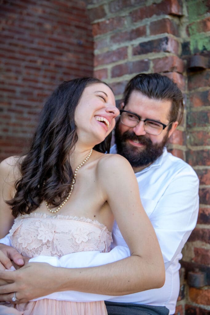 An engaged couple embrace and laugh at the red bricks at Max's Garden in Dumbo, Brooklyn, NYC.