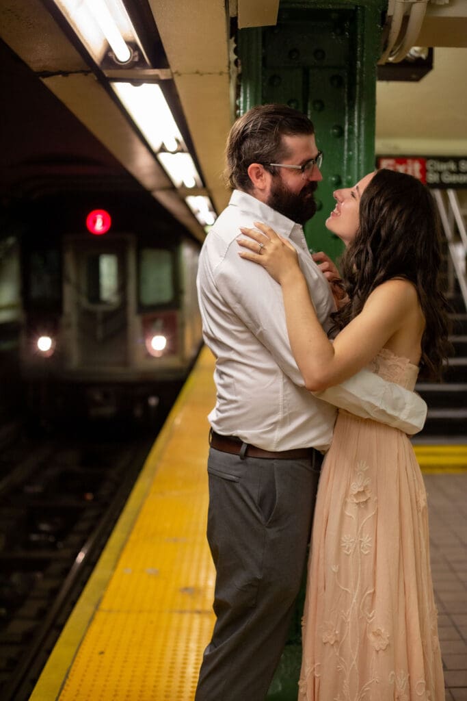 An engaged couple embraces on a Brooklyn subway platform as a train approaches.