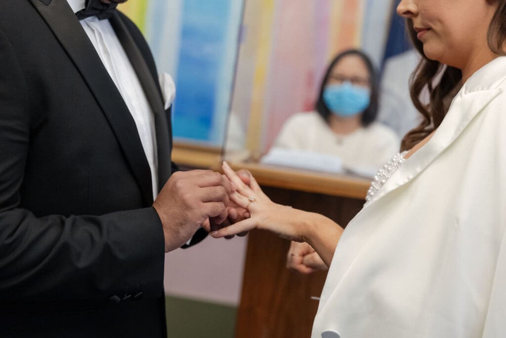 Newlywed couple exchange rings while getting married in the pink ceremony room at NYC City Hall.