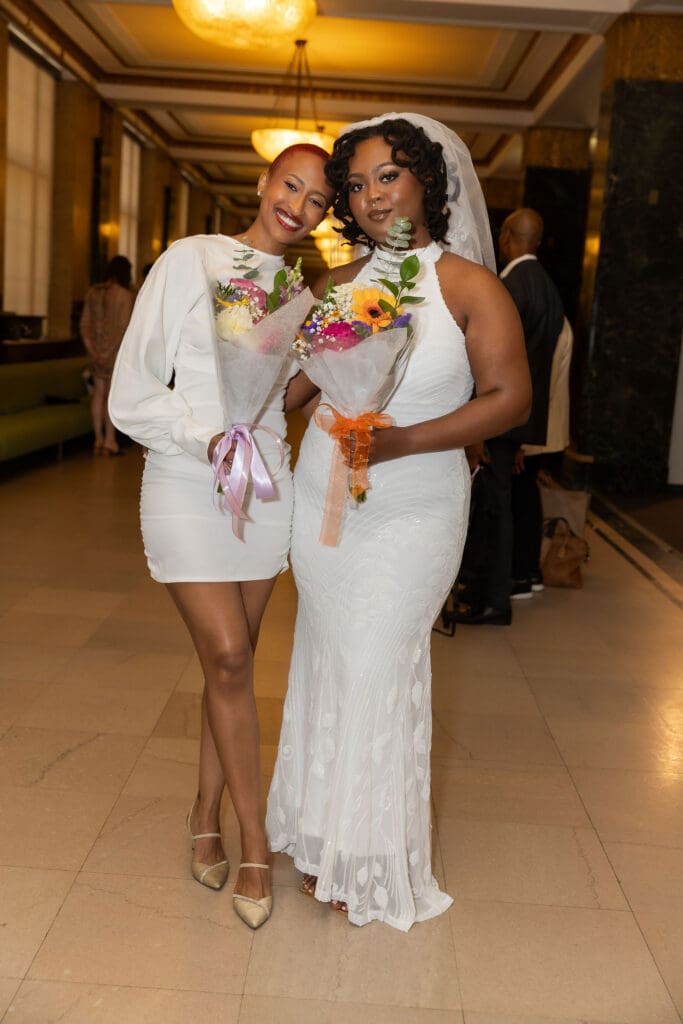 Two brides smile while waiting to get married at NYC City Hall.