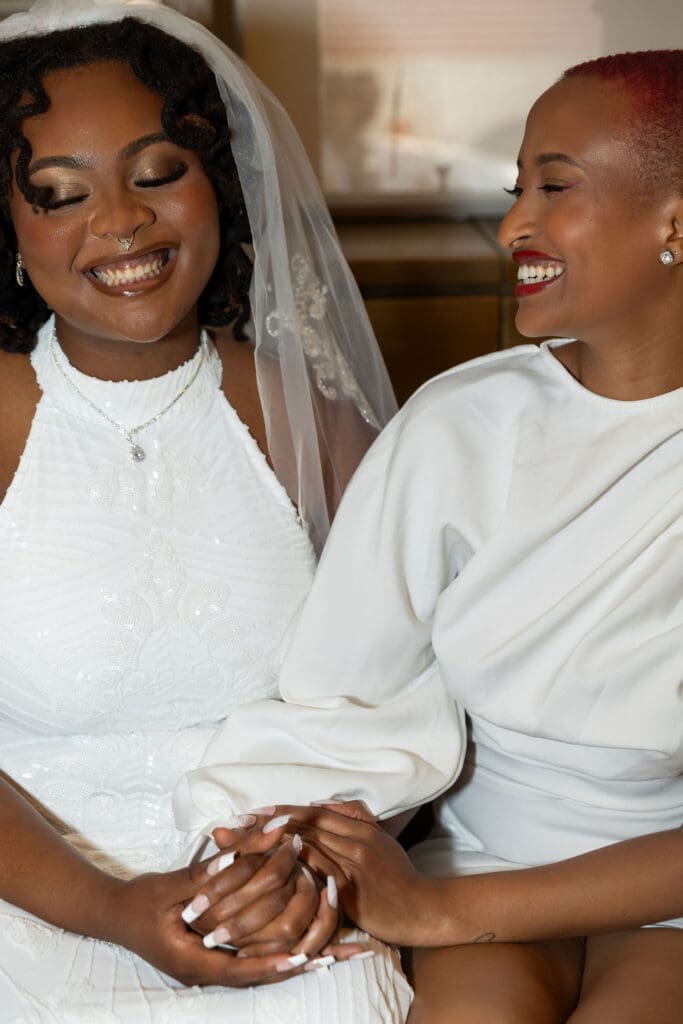 Two brides smile at the green couches while waiting to get married at NYC City Hall.