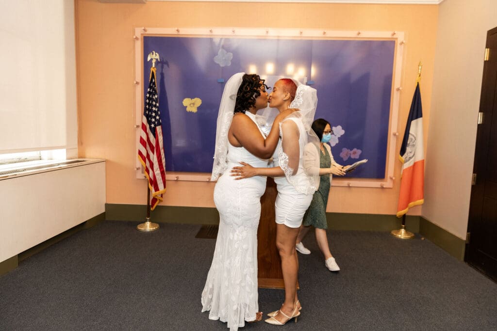 Two brides kiss after getting married in the blue ceremony room at NYC's City Hall.