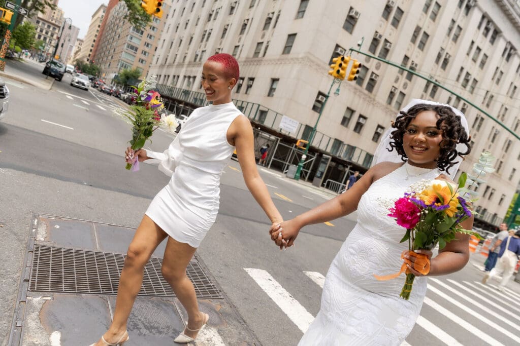 Two brides walk across the street in NYC after getting married at City Hall.
