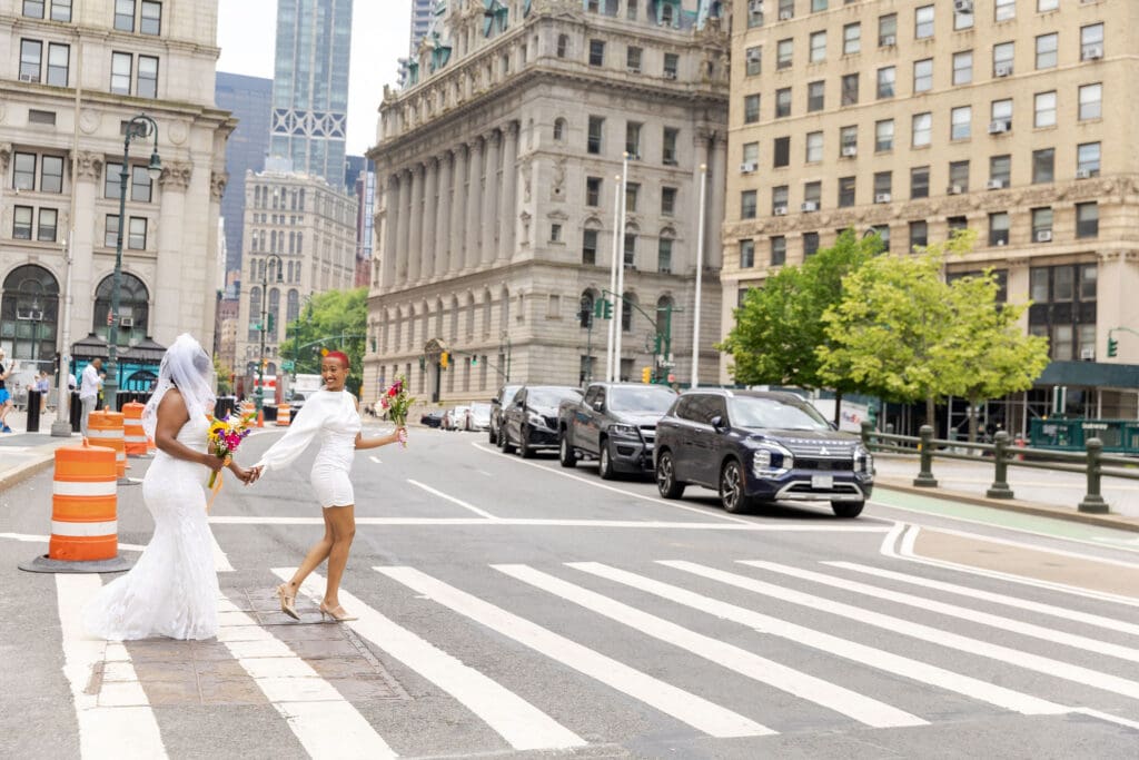 Two brides walk across a NYC street after getting married at City Hall.
