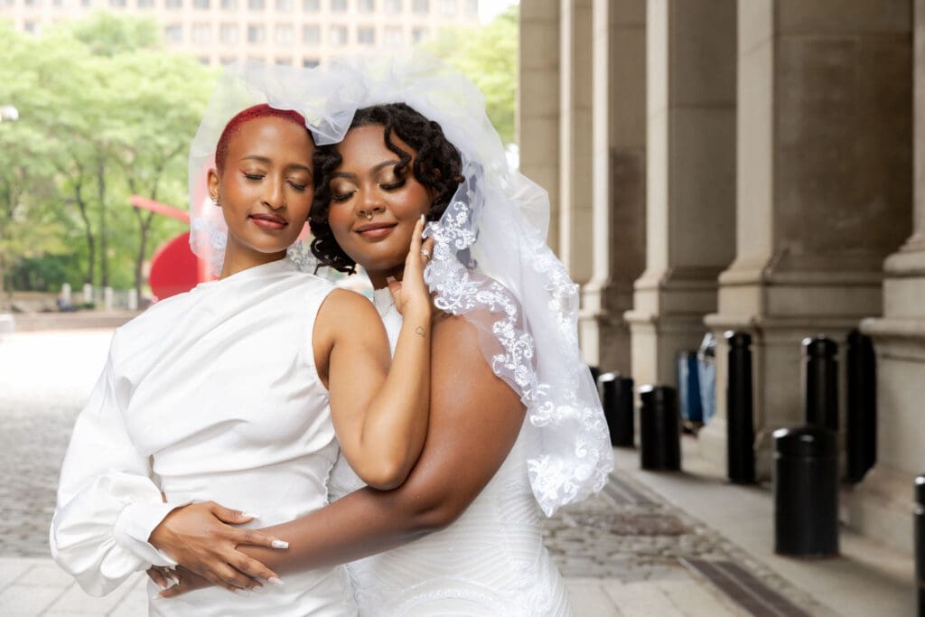Two brides embrace with their eyes closed in NYC after getting married at City Hall.