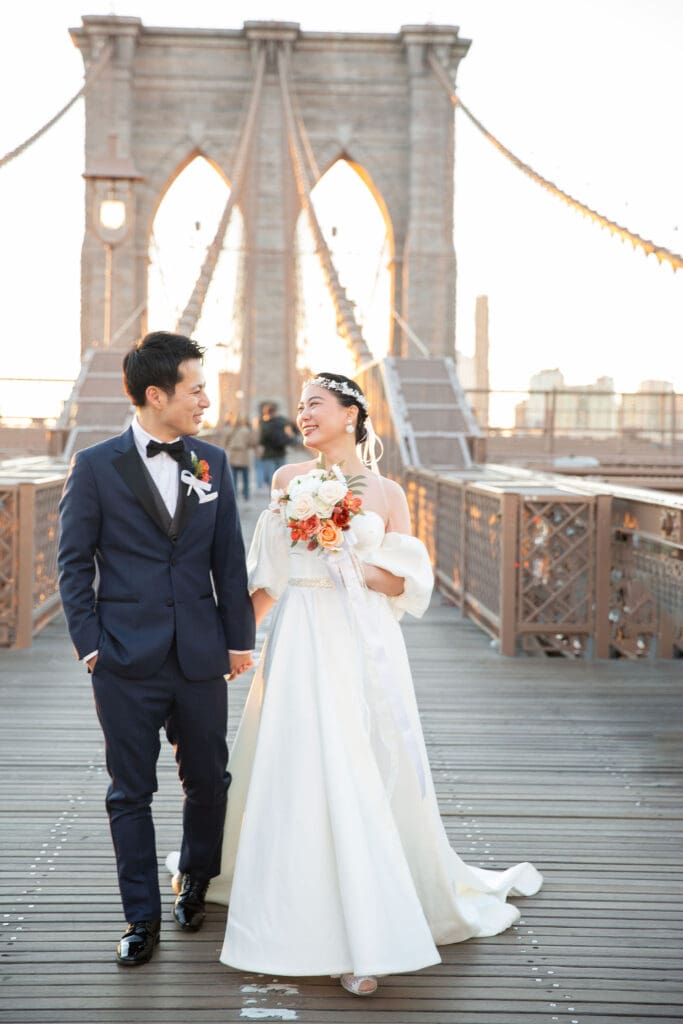 Newlyweds laugh and walk around at the Brooklyn Bridge in NYC.