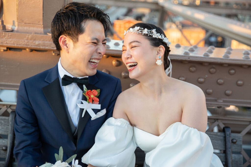 Newlyweds laugh at Brooklyn Bridge in NYC.