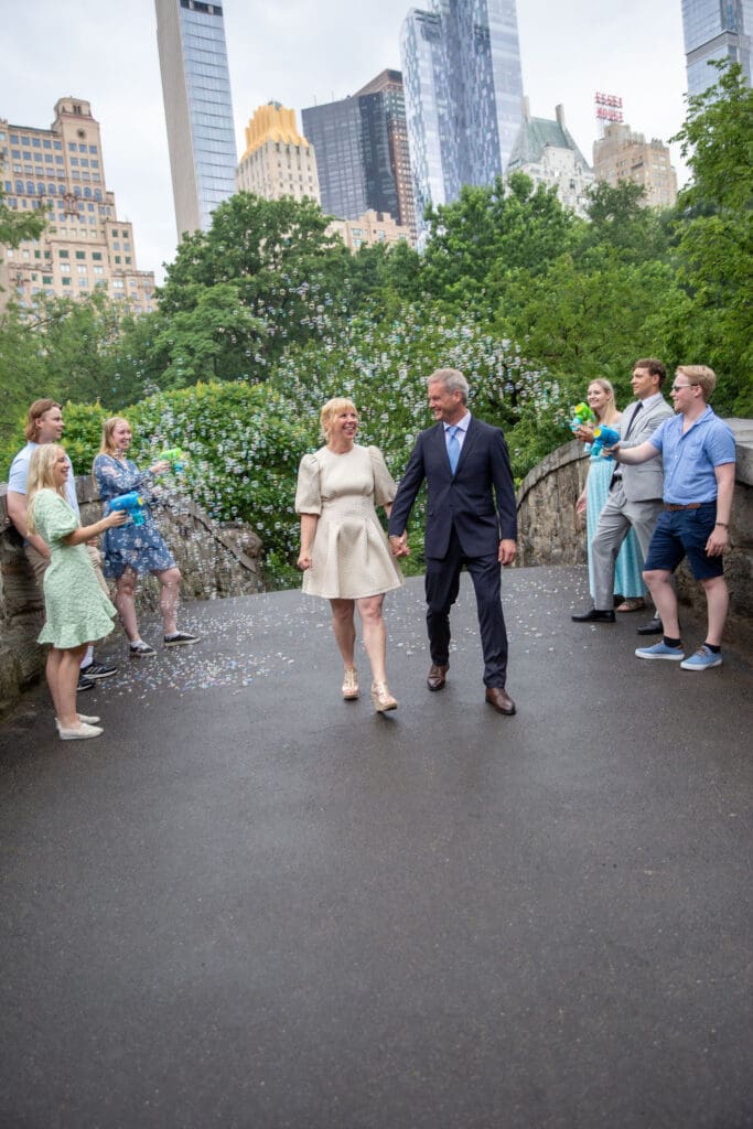 NYC Elopement in Central Park after after ceremony at the Norwegian Seamen's Church. Family blows bubbles at Bride and groom at Gapstow Bridge.