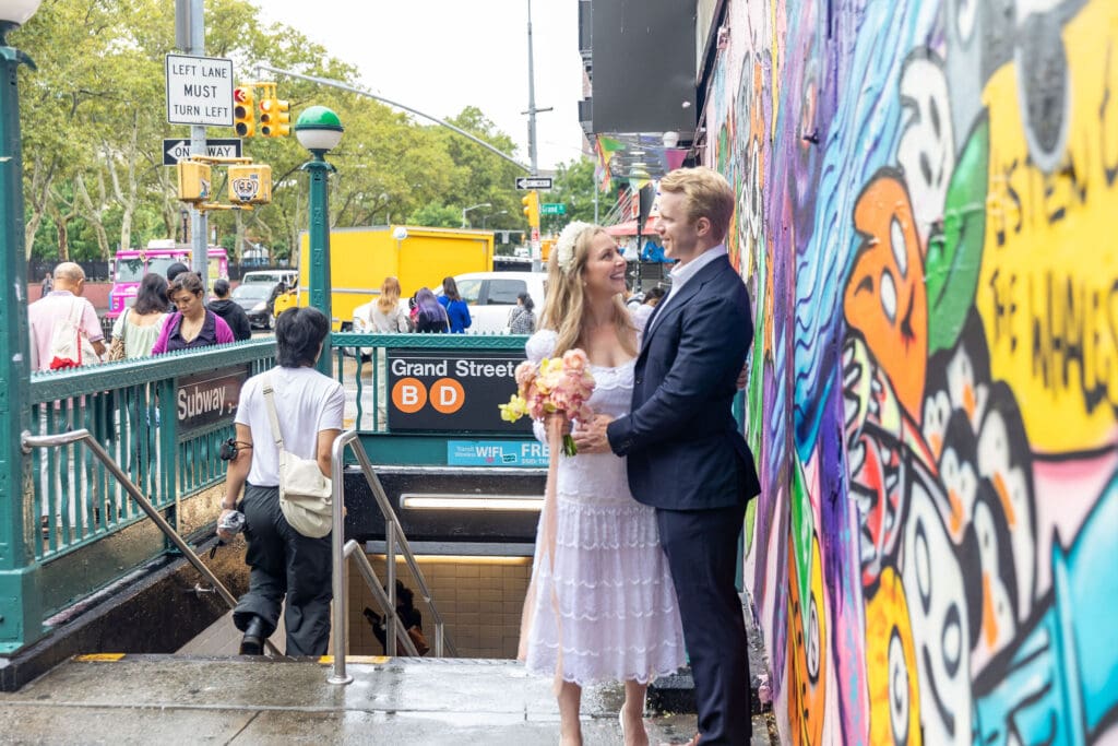 Newlyweds take wedding portraits in front of graffiti and Grand St Subway station in Chinatown NYC.