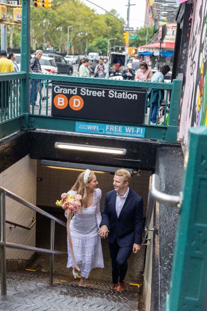 Newlyweds take wedding portraits walk up steps of Grand St Subway station in Chinatown NYC.