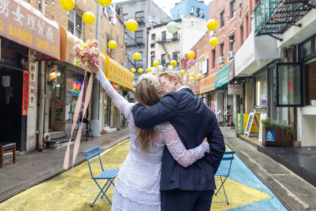 Newlyweds kiss during wedding portraits in Chinatown NYC on Doyers Street with lanterns in background.