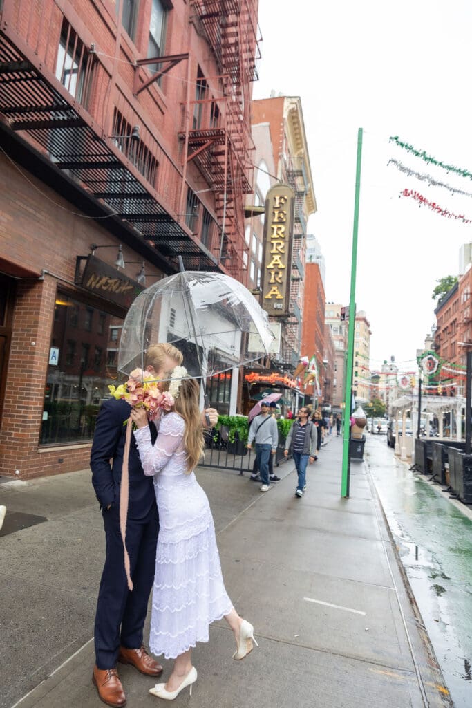 Newlyweds kiss during wedding portraits in Little Italy NYC with Ferrara's in the background.