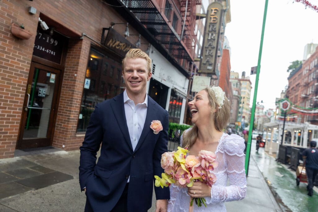 Newlyweds laugh during wedding portraits in Little Italy NYC with Ferrara's in the background.