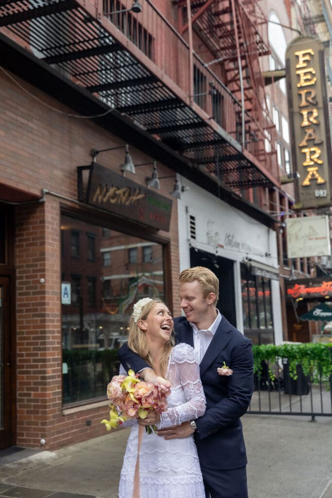 Newlyweds laugh during wedding portraits in Little Italy NYC with Ferrara's in the background.