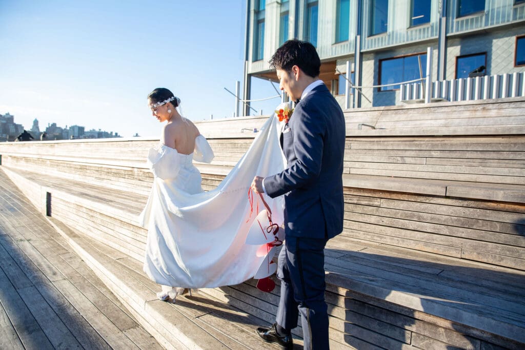 Newlyweds walk around South Street Seaport during a wedding portrait session in NYC. Groom carries bride's train.