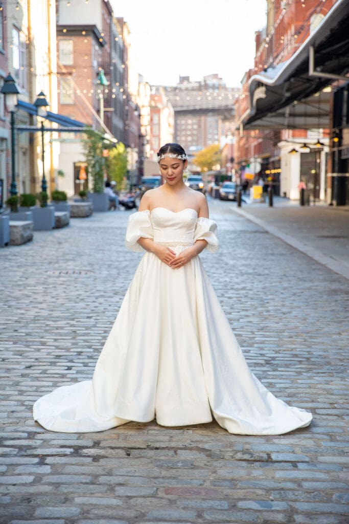 Bride poses for a solo photo with South Street Seaport in NYC behind her.