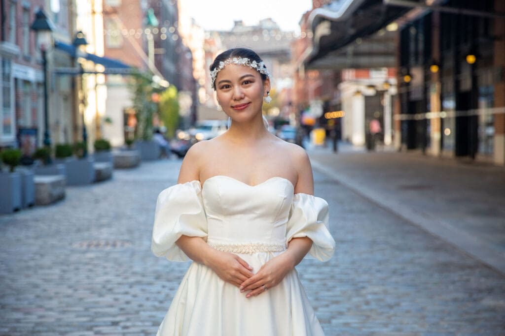 Bride poses for a solo photo with South Street Seaport in NYC behind her.