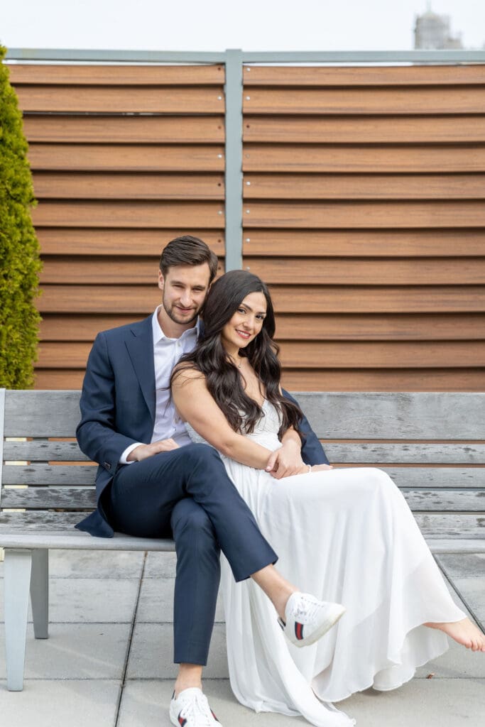 Engaged couple relax on their rooftop on the Upper West Side with a view of Manhattan behind them.