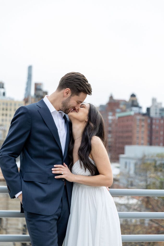 Engaged couple kiss on their rooftop on the Upper West Side with a view of Manhattan behind them.