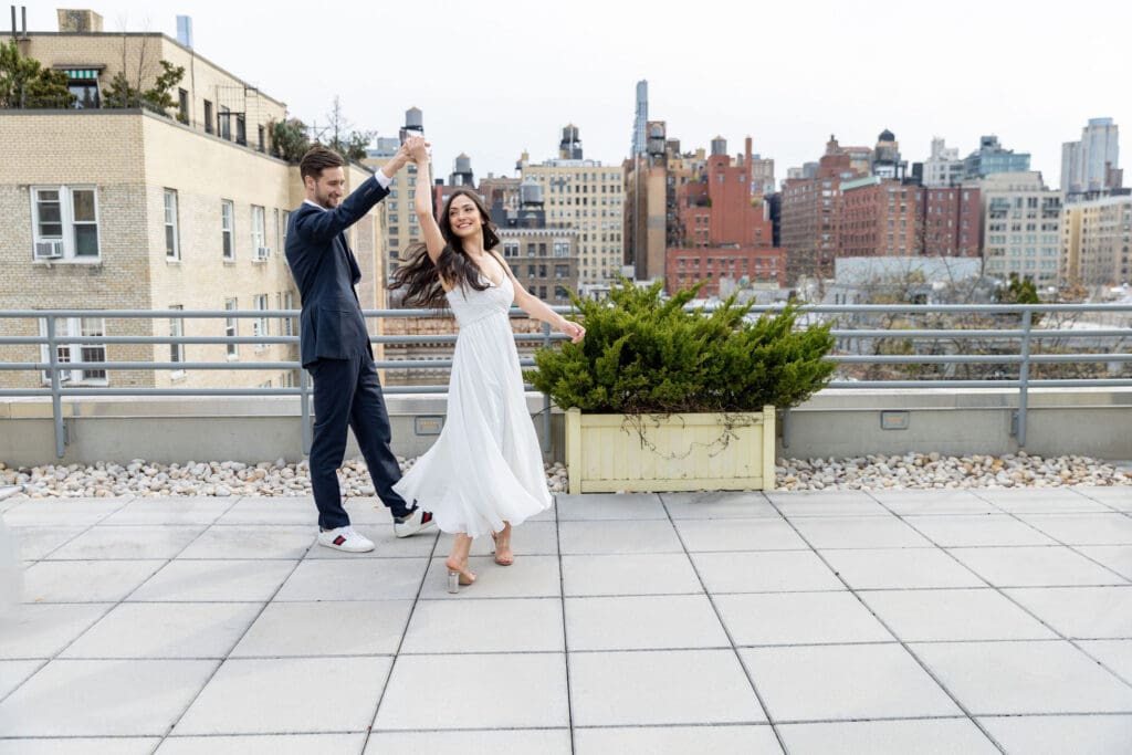 Engaged couple dance on their rooftop on the Upper West Side with a view of Manhattan behind them.
