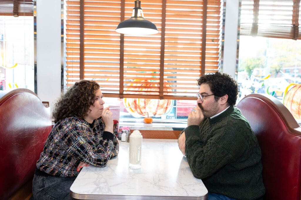 Engaged couple blow straws at each other at Bel-Aire Diner in Astoria, Queens during their casual pre-wedding portrait session in NYC.