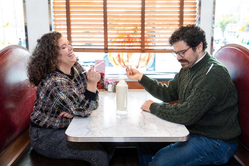Engaged couple enjoy milkshakes in at Bel-Aire Diner in Astoria, Queens during their casual pre-wedding portrait session in NYC.