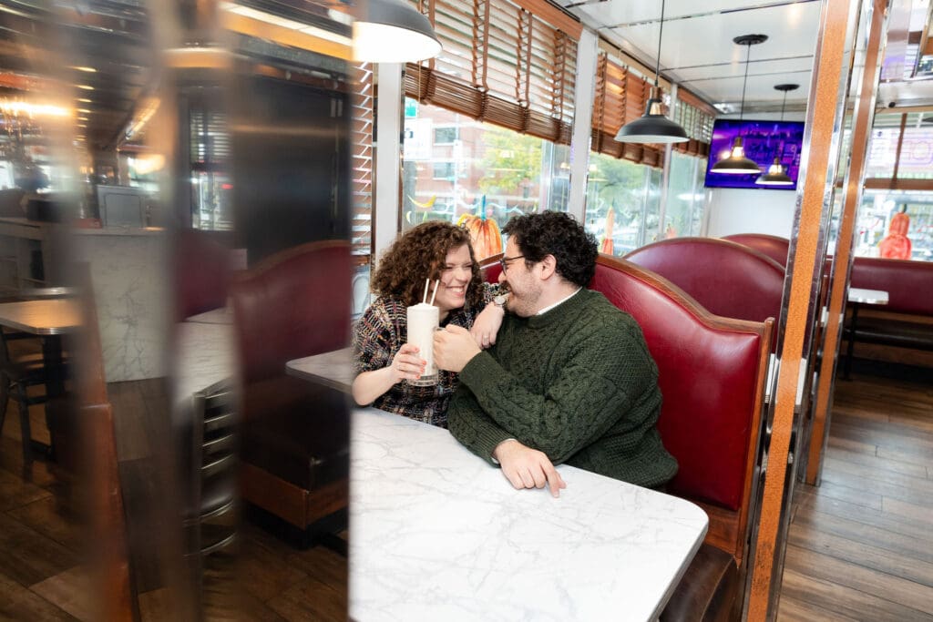 Engaged couple enjoy milkshakes in at Bel-Aire Diner in Astoria, Queens during their casual pre-wedding portrait session in NYC.