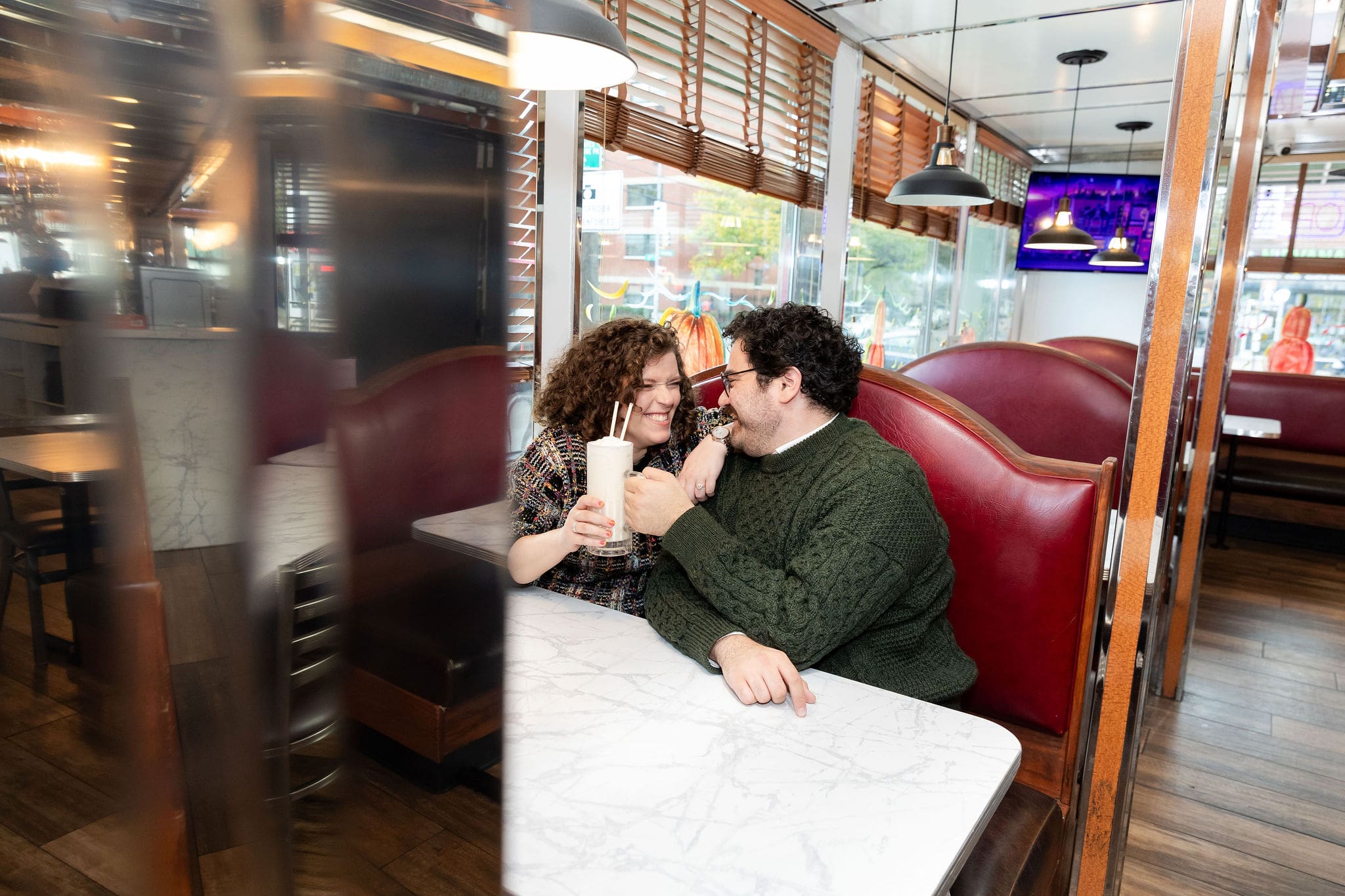 Engaged couple enjoy milkshakes in at Bel-Aire Diner in Astoria, Queens during their casual pre-wedding portrait session in NYC.