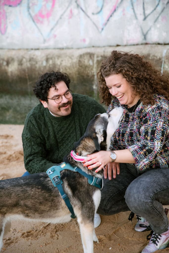 Engaged couple play with a dog at sunset at Hallett's Cove in Astoria, Queens for their fall engagement session.