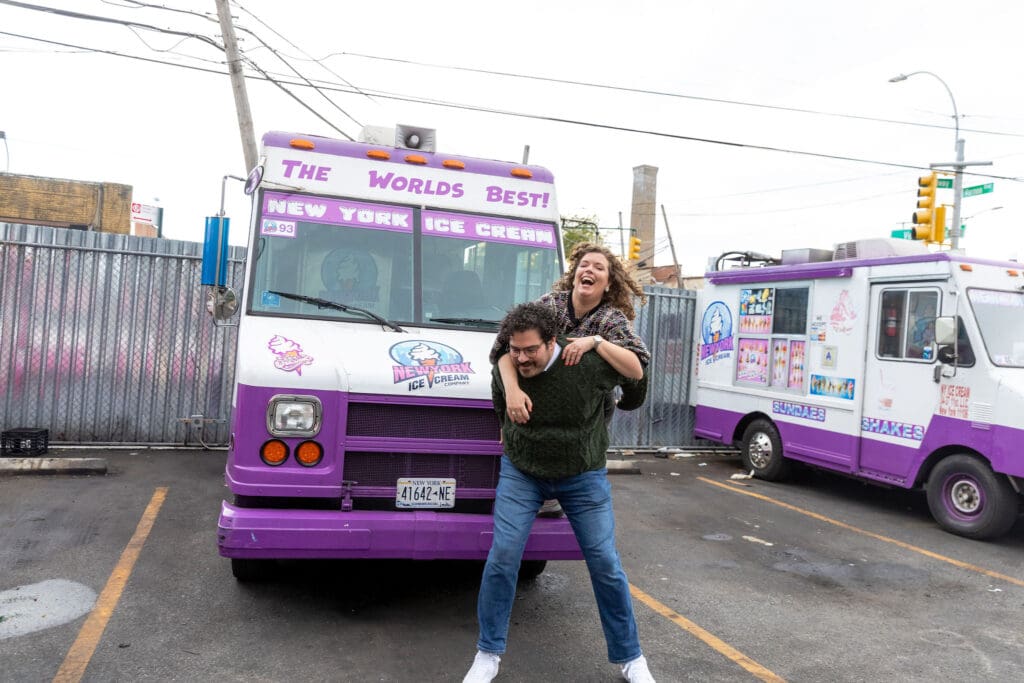 Engaged couple do a piggy back ride near ice cream trucks in Astoria, Queens for their fall engagement session.