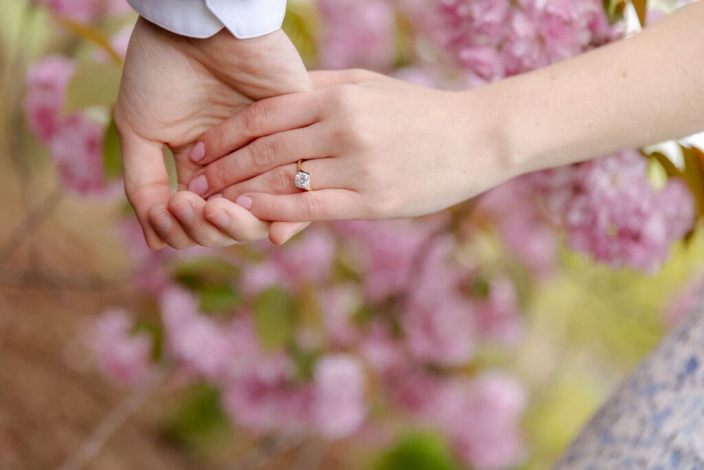 Close up of hands holding engagement ring with cherry blossoms in the background in Central Park.